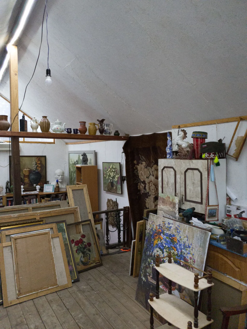 An attic room stacked with framed paintings, ceramics, an old cabinet and decades of stored household belongings