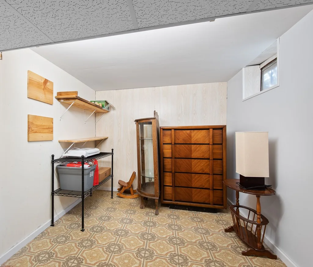 A finished basement holding a dated wooden dresser, a curio cabinet, a side table and shelved storage bins