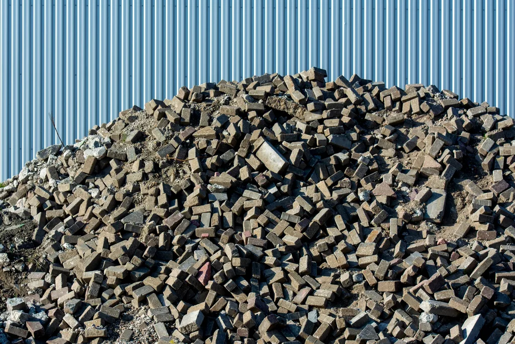 A large pile of broken paving bricks, concrete and rubble heaped against a corrugated steel wall