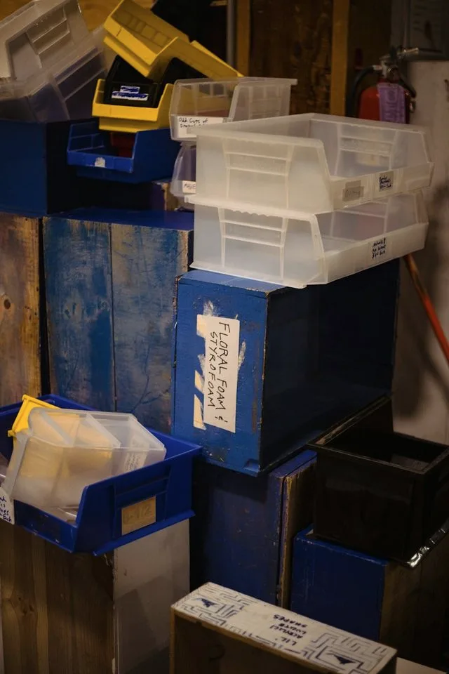 Plastic storage bins and wooden crates stacked several deep, each hand-labelled with its contents