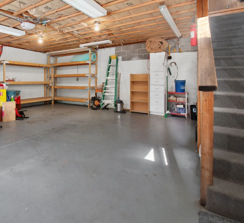 An attached residential garage with timber storage shelving, a step ladder, cabinets and a concrete floor