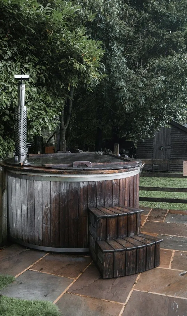 An old wooden hot tub with a closed lid and timber steps, standing on a back garden patio